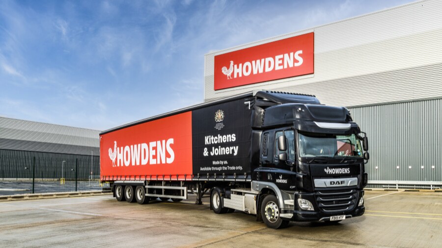 Howdens delivery lorry, featuring large logo and royal warrant seal, in an industrial car park.