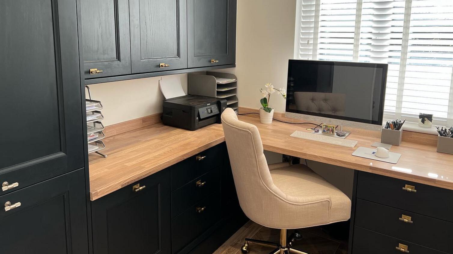 Navy shaker home office design with brass antique handles, a cream office chair, solid wood worktops, and a silver computer.