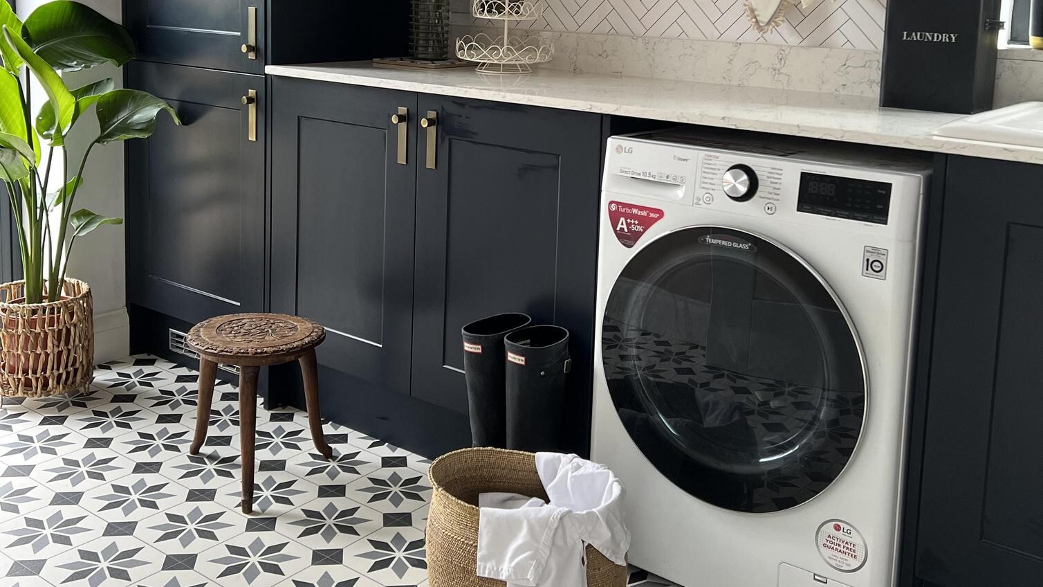 On-trend utility room idea using navy shaker units, white quartz worktops, brushed-brass handles and rectangular backplates.