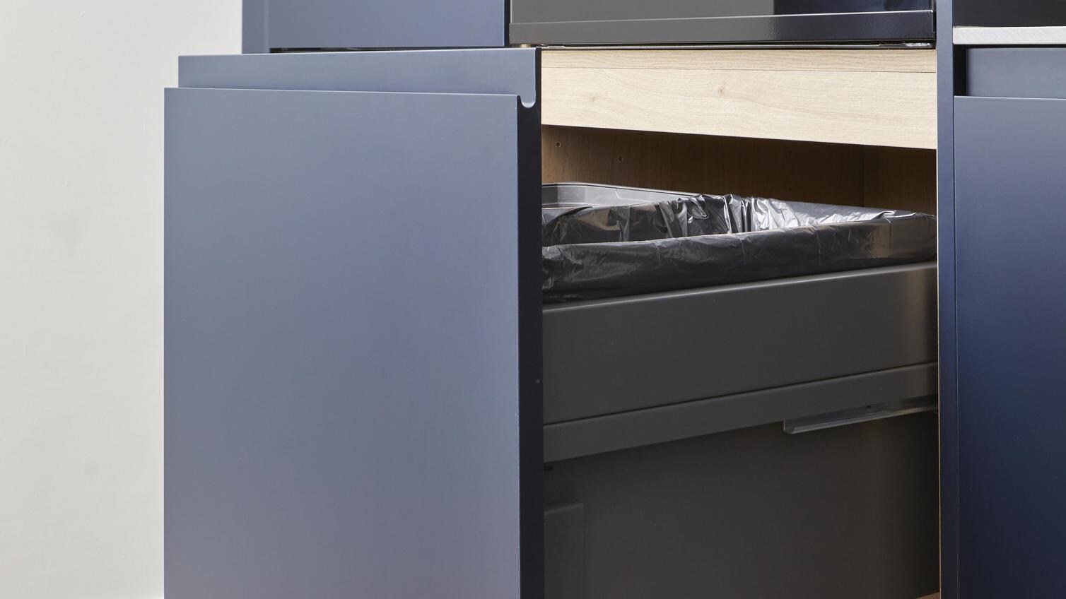 Double-compartment bin, integrated behind a navy kitchen door and with sections for waste and recycling.
