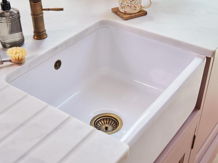 A white worktop with a belfast kitchen sink fitted underneath. The sink has a brass waste and strainer and matching overflow