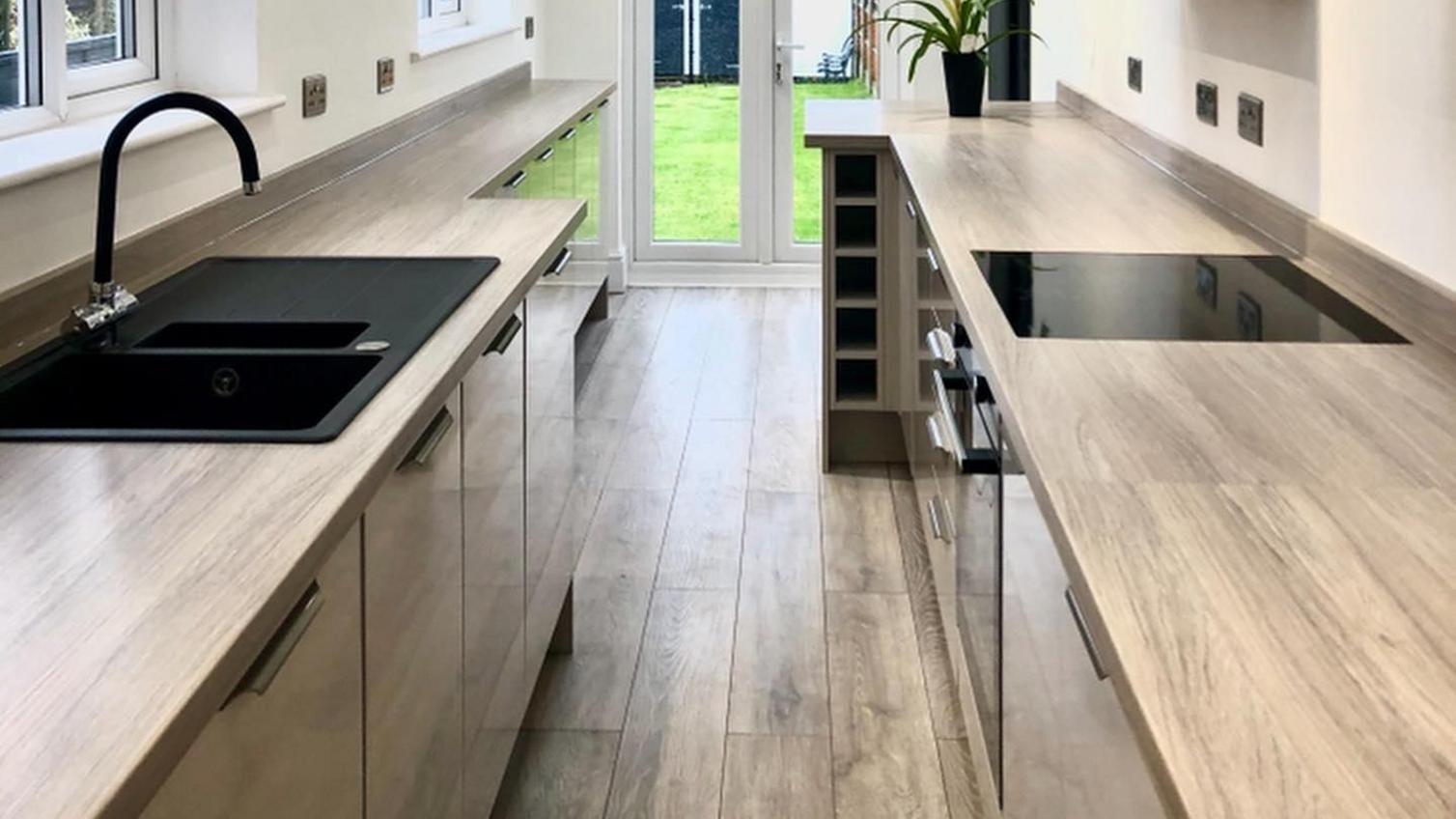 Cream glossy slab kitchen in a galley layout. Has a black single bowl sink and tap, a black inductive hob, and a wine rack.