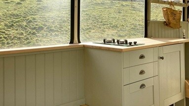 Sage green kitchen on a single wall design in a bus, with chrome cup handles, large windows, and wall panelling.