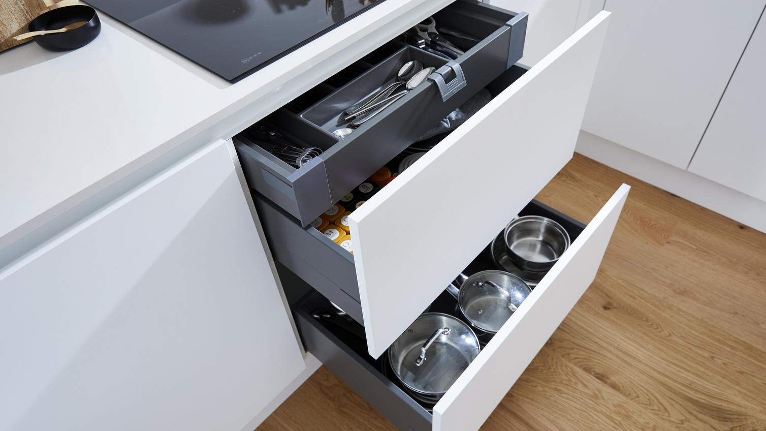 A compact white kitchen with two pan drawers and cutlery tray fitted beneath a black induction hob.