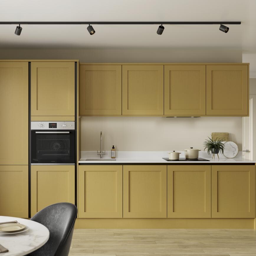A handleless painted shaker kitchen in mustard yellow with black profiles. Includes white worktops and pale timber floors.