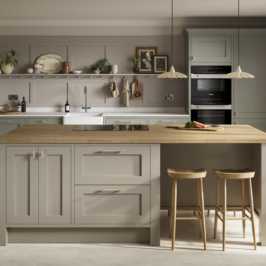 A green kitchen with shaker doors in an island layout. Has oak worktops, open shelving, and stone floors for an earthy design