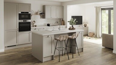 A pebble-coloured shaker kitchen with a single wall layout and a central island. There are white worktops and wood flooring.