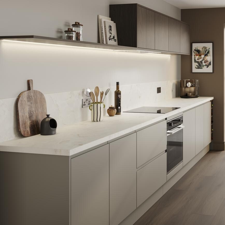 A sand grey, integrated handle kitchen in a galley layout. There are white worktops, white sinks, and dark plank flooring.