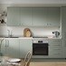 A gloss, reed green kitchen in a single wall layout. It has grey worktops, stainless steel sink, and integrated oven.