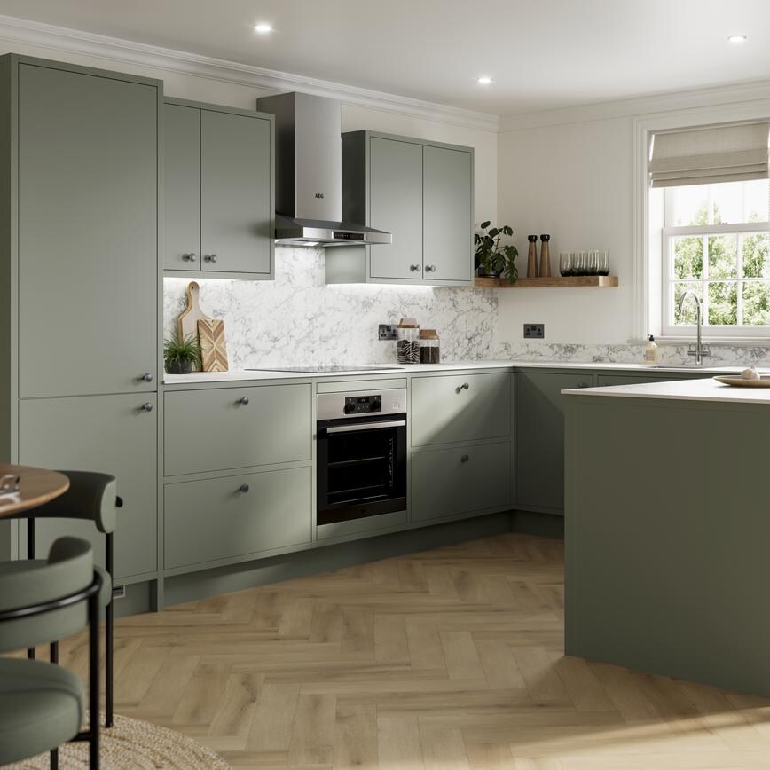 Green peninsula kitchen with matt finish and in-frame cabinet design. Features white counters and marble-effect splashback.