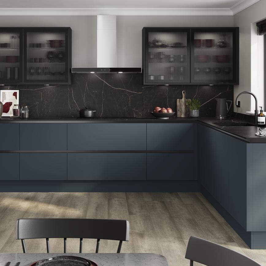 A marine blue handleless kitchen idea in a u-shaped layout. Has black profiles, fluted glass cupboards, and black worktops.