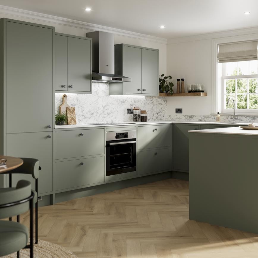 Green peninsula kitchen with matt finish and in-frame cabinet design. Features white counters and marble-effect splashback.
