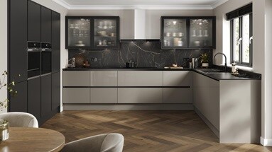 A handleless, l-shaped kitchen in a sand grey finish. There are fluted glass wall units and oak-style herringbone flooring.