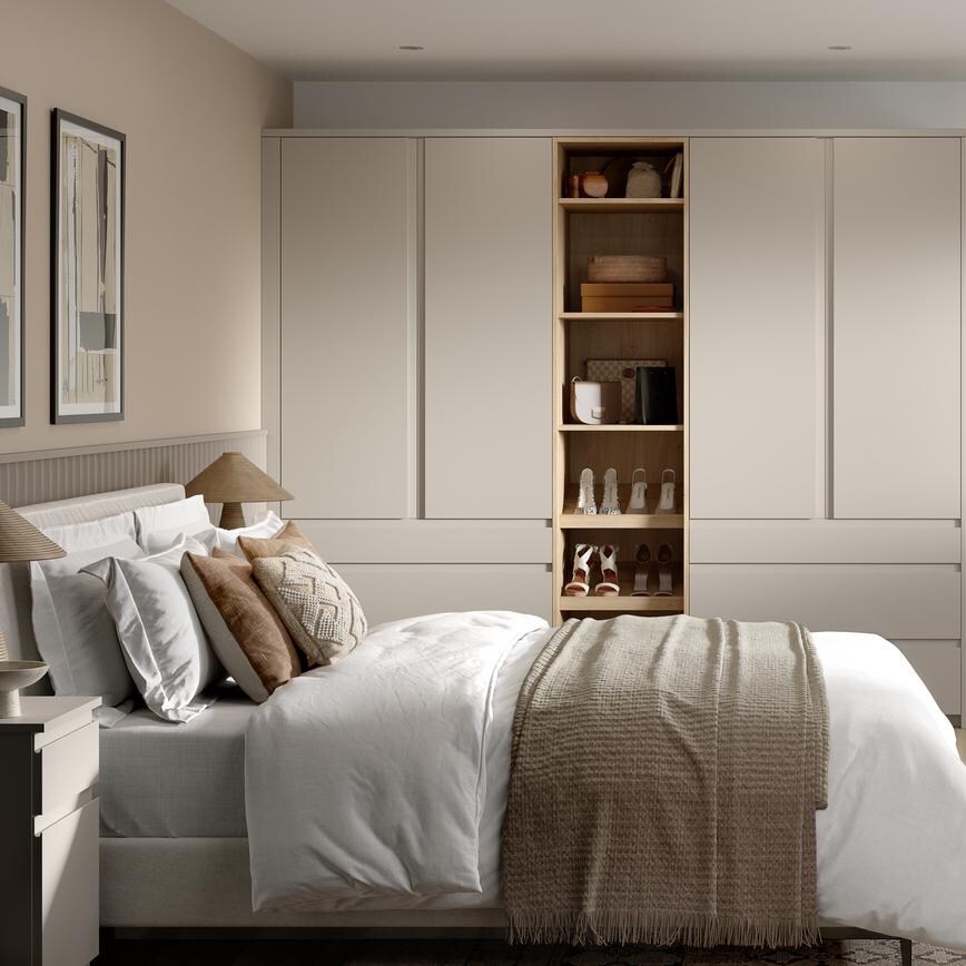 A matt sandstone bedroom with tall wardrobes and matching drawers. It has shelves in between and light, oak-style flooring.